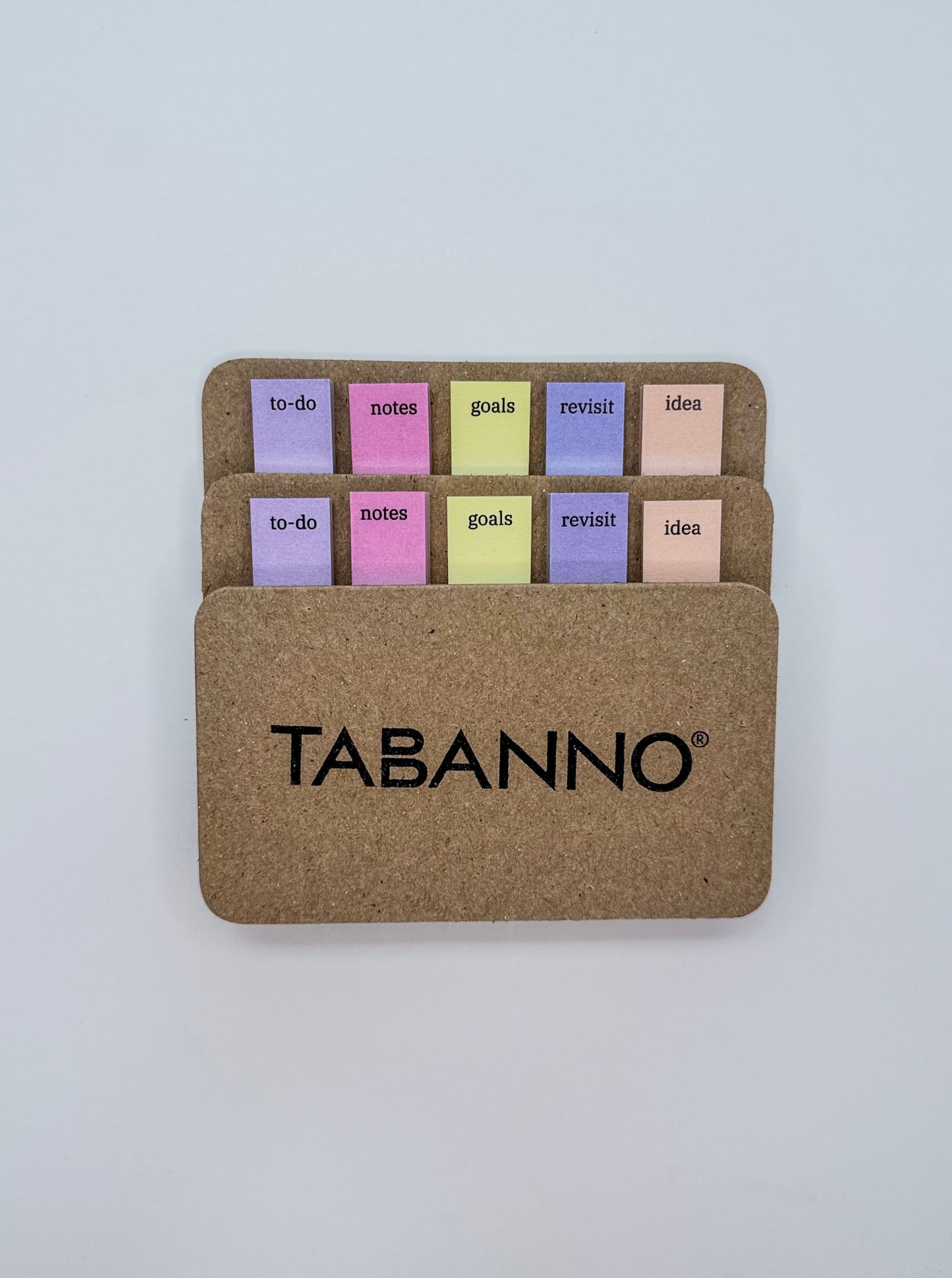 A cardboard-style notepad holder with the brand name TABANNO printed in black on the front. Inside, 5 pastel-colored sticky notes in purple, pink, yellow, and peach are arranged in two rows against a plain light gray background.